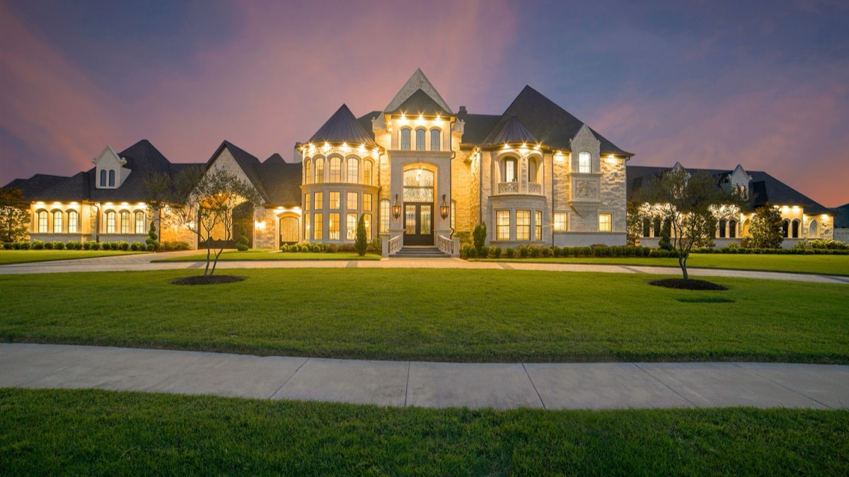 An illuminated country house at dusk, seen from the drive.
